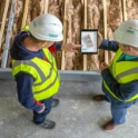Two construction workers review plans on a tablet.